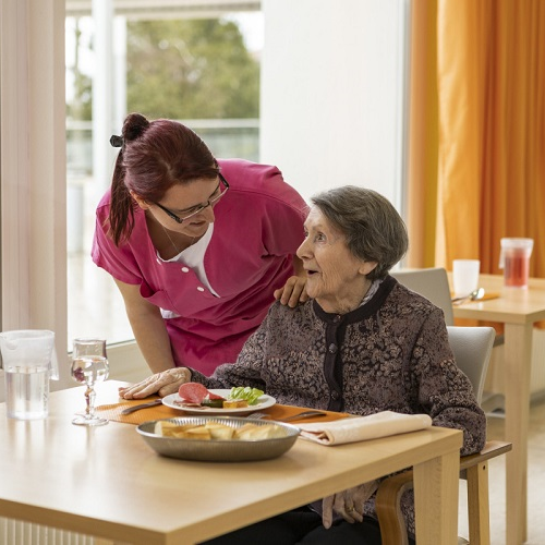 En äldre kvinna blir serverad mat av Sodexo-medarbetare