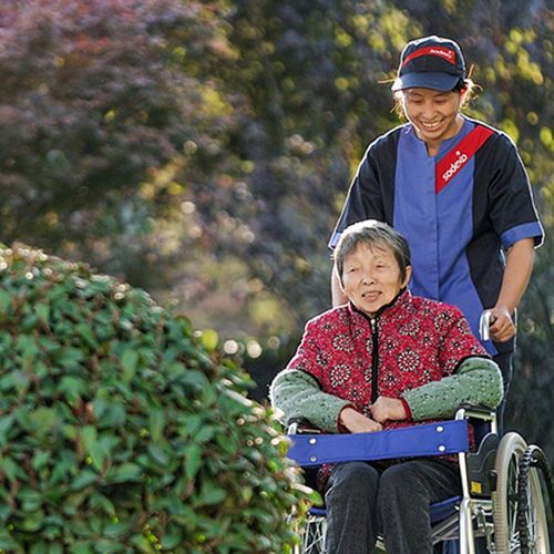 Sjuksköterska från Sodexo promenerar med en äldre kvinna i rullstol